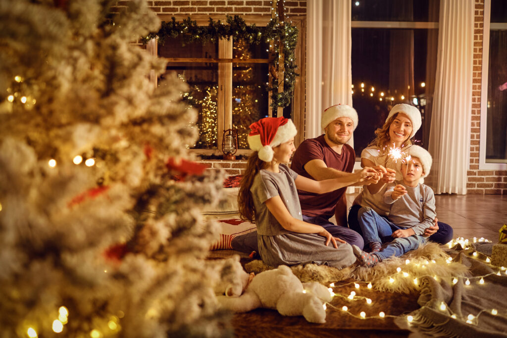 Ģimene ar diviem bērniem svin Ziemassvētkus izrotātā mājā ar siltām gaismiņām