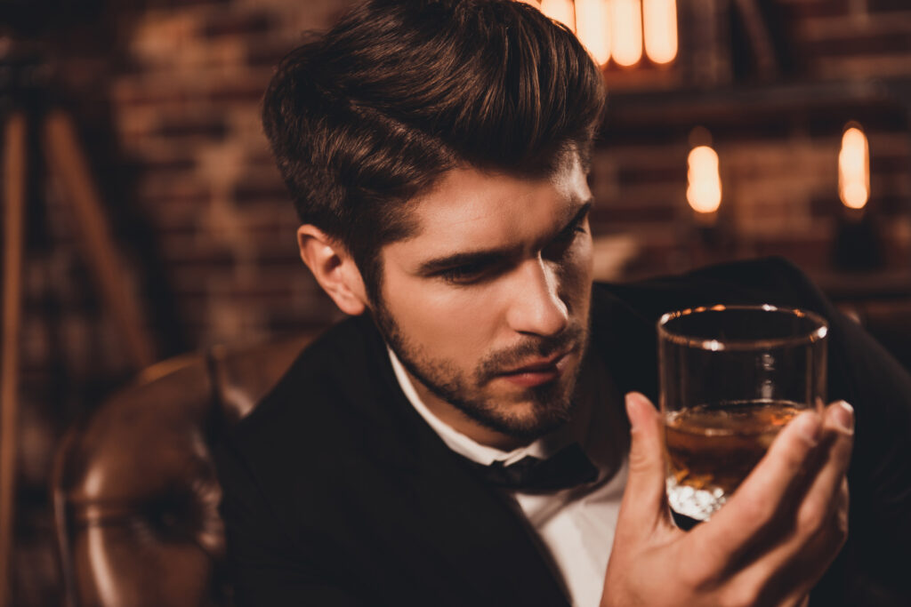 Jauns vīrietis uzvalkā pēta glāzi viskija vai konjaka