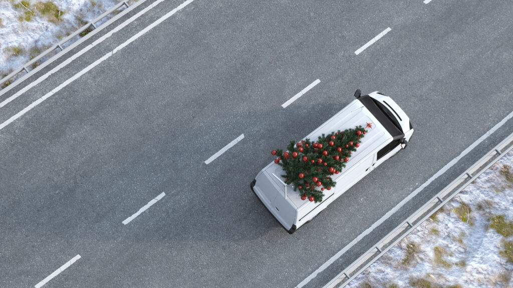 Balts busiņš jeb minivans brauc pa šoseju ar Ziemassvētku eglīti uz jumta
