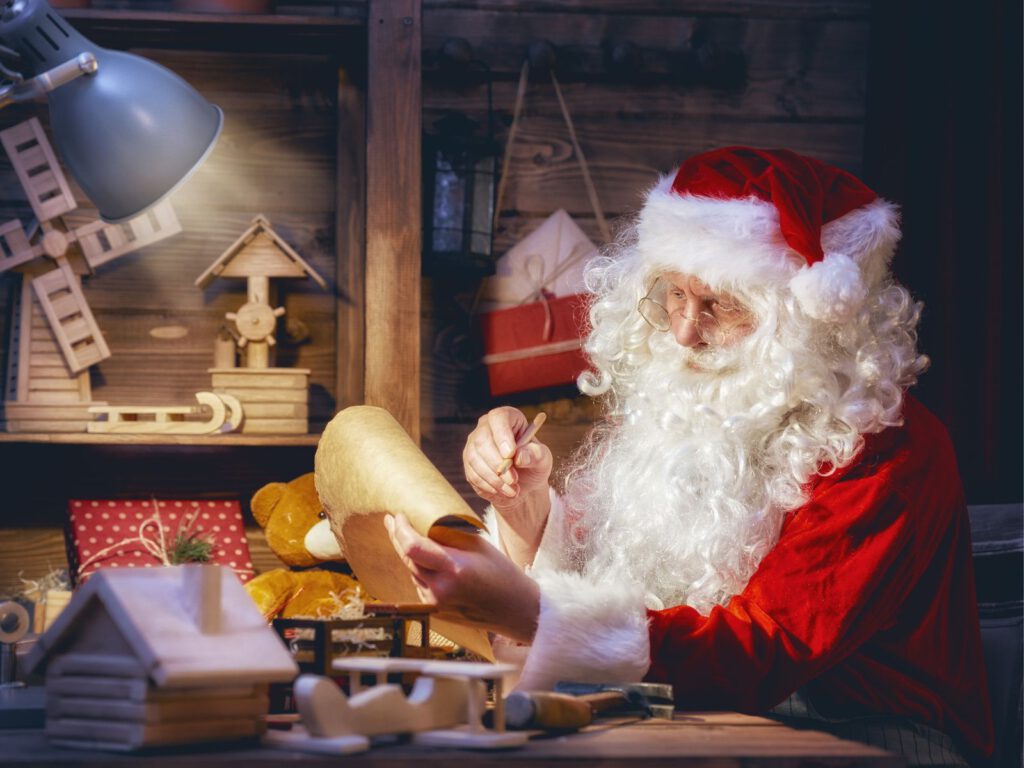 Дед Мороз готовит подарки и проверяет список детей у себя дома, в мастерской.