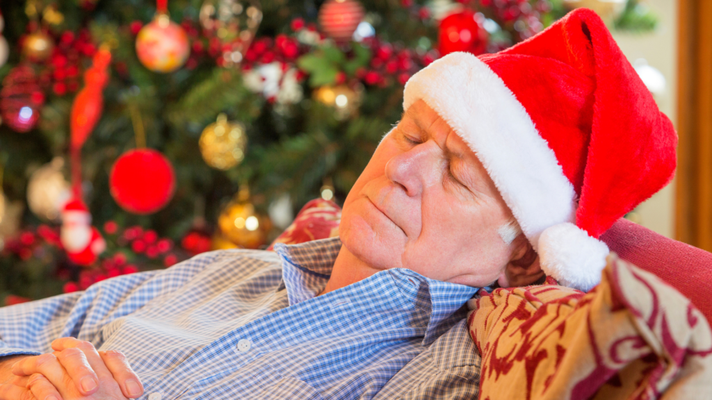 Vectēvs - vecs vīrietis guļ Ziemassvētku cepurē pie eglītes
