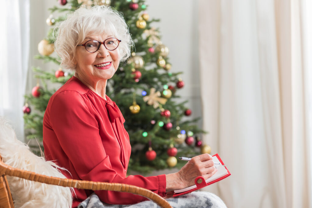 Vecmāmiņa sēž krēslā pie Ziemassvētku eglītes